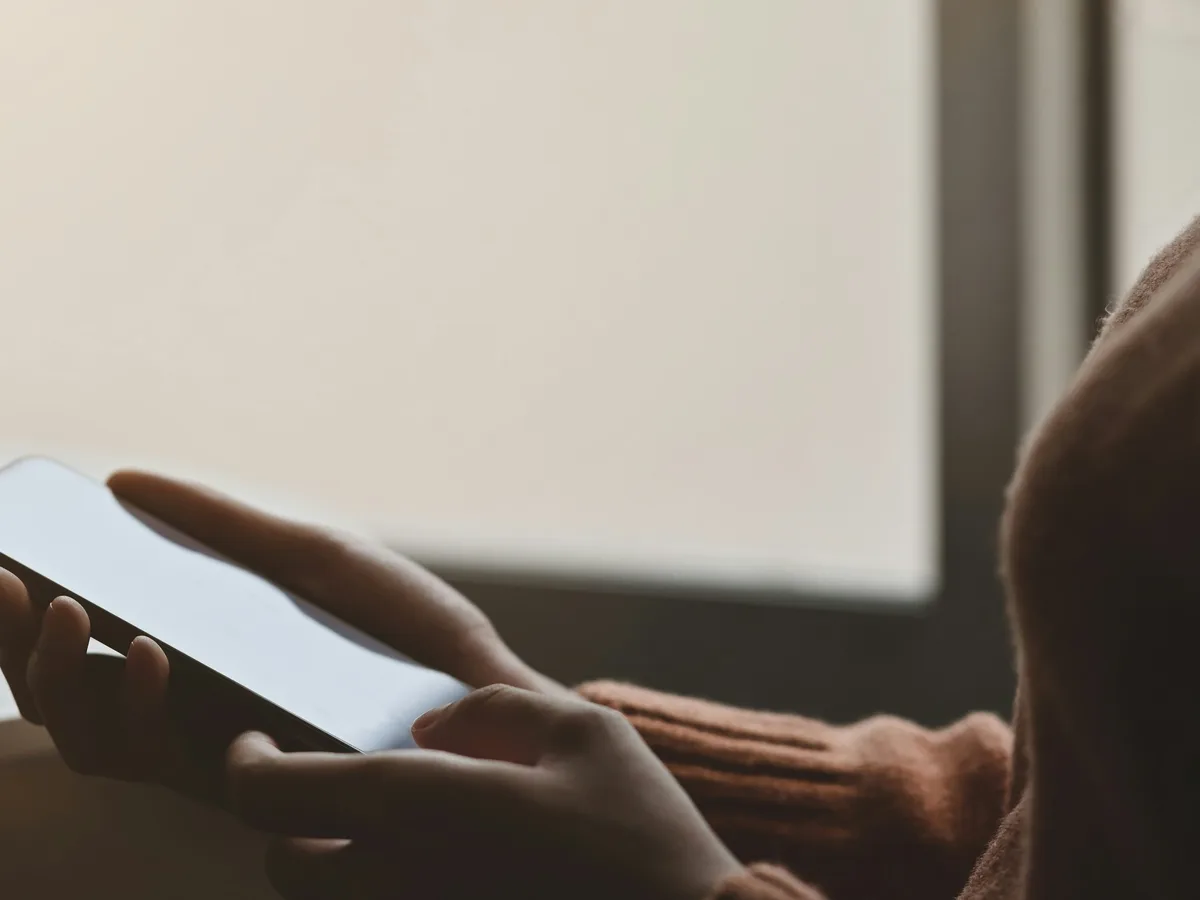 Osoba korzysta z telefonu przy oknie, obok leży notes z codziennymi obserwacjami