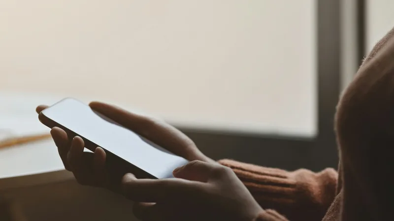 Osoba korzysta z telefonu przy oknie, obok leży notes z codziennymi obserwacjami